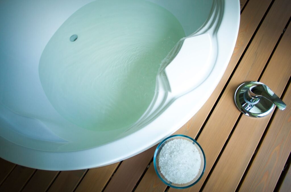A white bathtub filled with water beside a glass bowl of white crystals, the setup a strip soak actually uses