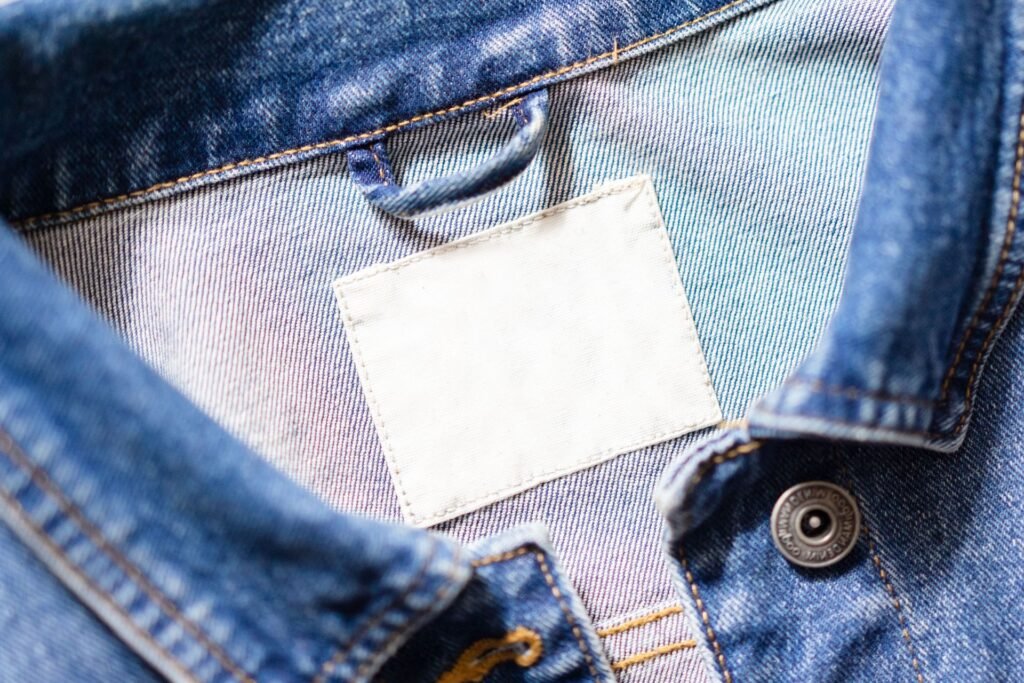 A blank white care tag sewn into the collar of a denim jacket, the label every washing decision starts from