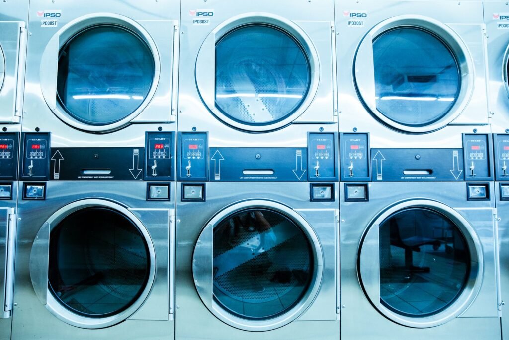Stacked commercial washing machines in a launderette, each with a small lit display above the door