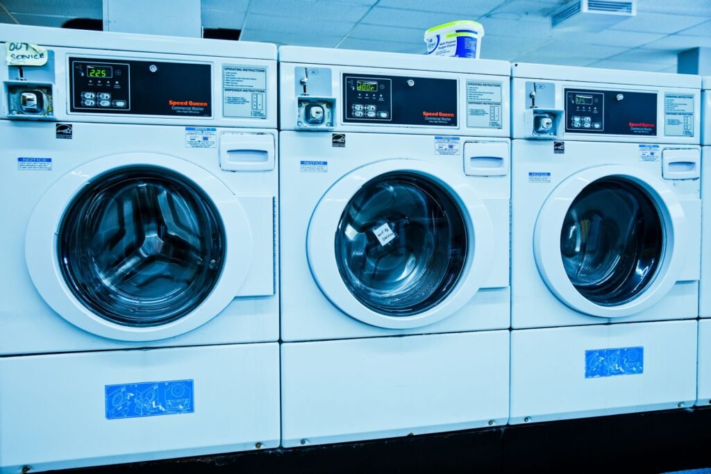 Three front-loading washers in a launderette with lit digital displays above their doors