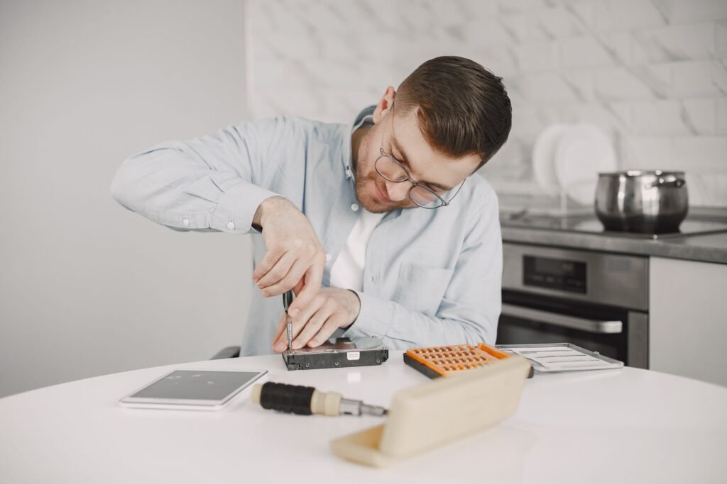 A man on the phone while opening an appliance with a screwdriver at a kitchen table, weighing a repair against a quote