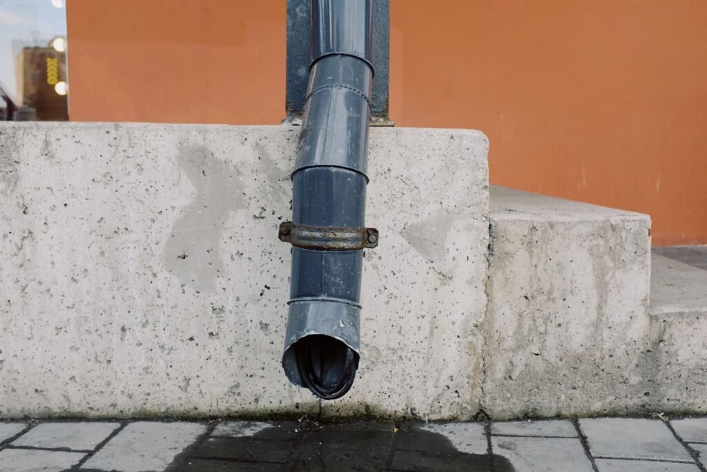 The open mouth of a drain pipe ending above a concrete step, the air gap that keeps drain smells out