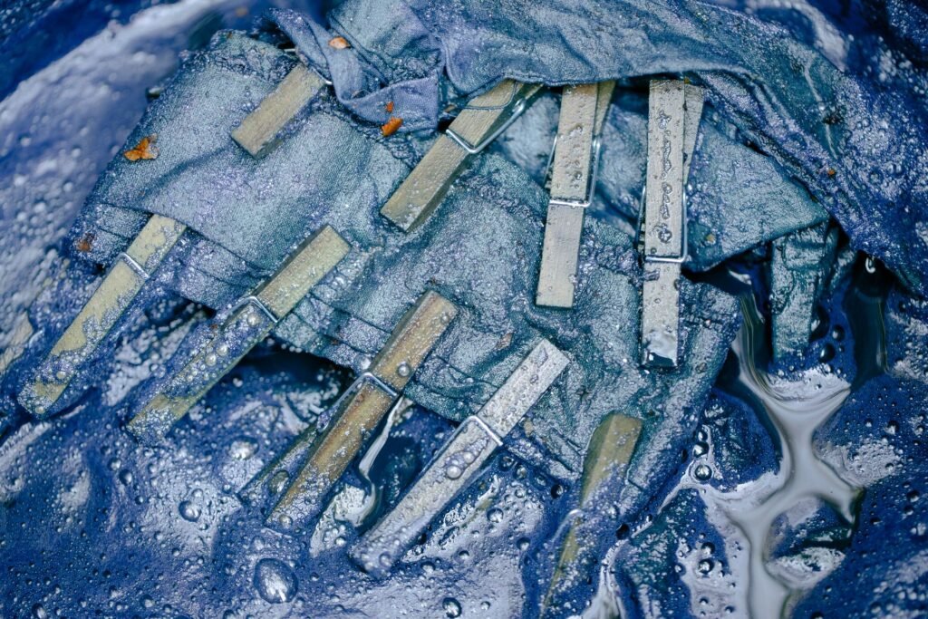 Wooden pegs on damp blue fabric with water still pooling around it, the standing moisture a musty washing machine smells of