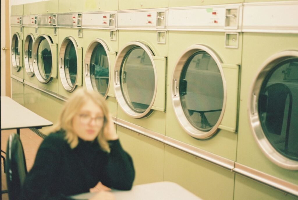 Woman sitting and waiting beside a row of front-load washers that have not moved on