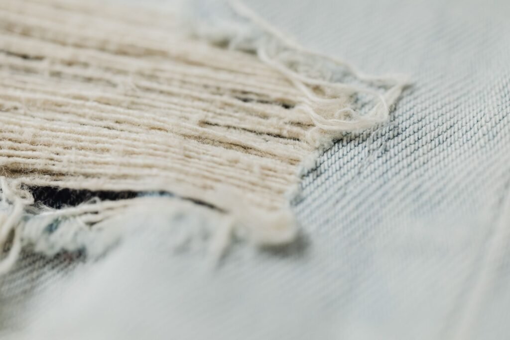 Macro view of a torn denim edge with broken and frayed threads, the kind of damage a snag inside a washer drum leaves