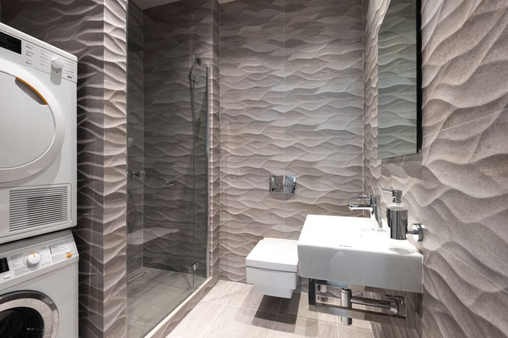 Stacked washer and dryer built into a modern bathroom, sharing the same supply pipework as the basin and shower