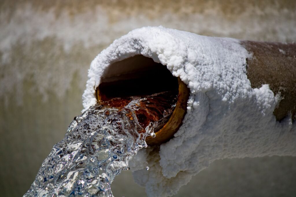 Water pouring from a pipe thickly crusted with white mineral deposits, what hard water leaves behind