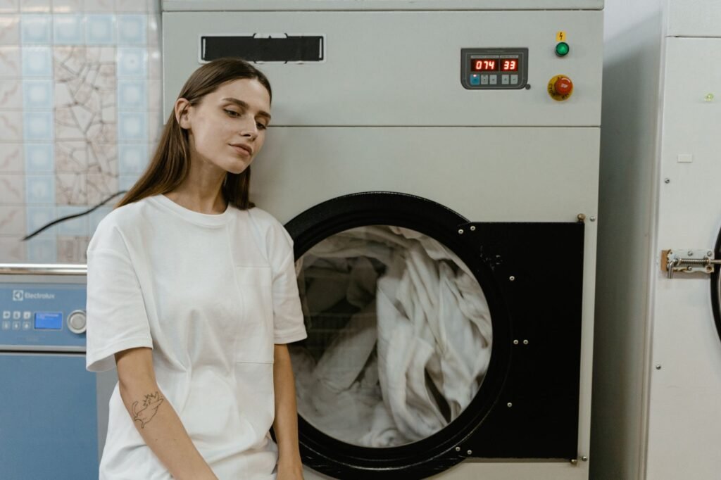 A woman standing at a front-load washing machine deciding which wash cycle to use