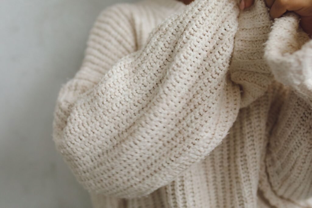 Hands holding a cream chunky-knit wool jumper, the fibre that felts and never comes back