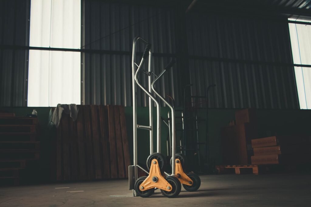 Two aluminium hand trucks parked in a dim warehouse, each fitted with orange three-spoke tri-star stair-climbing wheel clusters