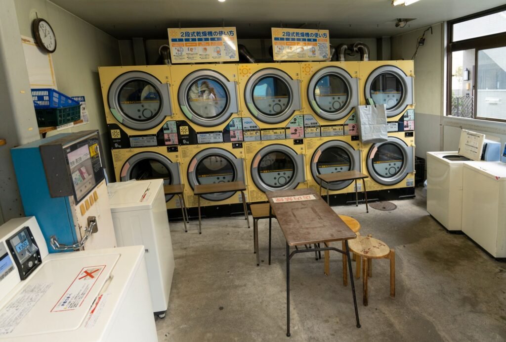 A small coin laundry with two rows of five stacked compact dryers, instruction placards above them and a folding table in the middle of the floor