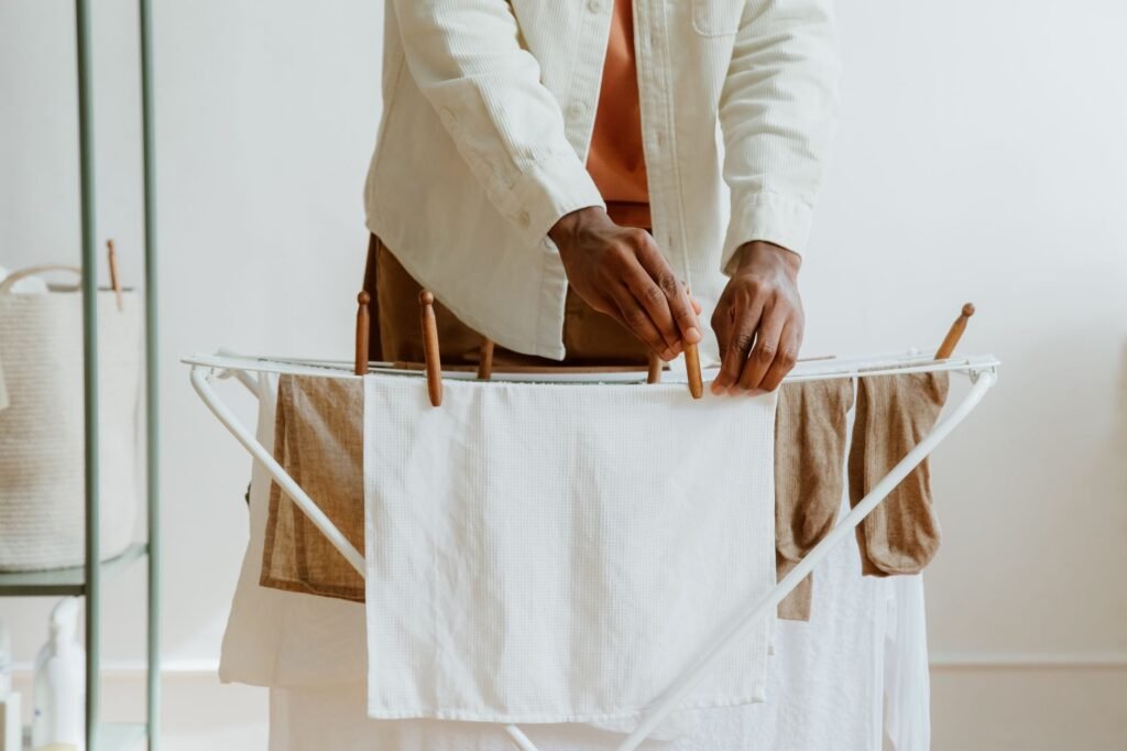 Hands pegging a white waffle towel onto a folding indoor drying rack hung with tan towels, the one alternative that removes the problem instead of treating it