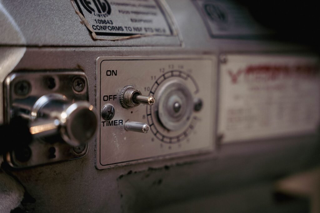 A worn metal machine control panel with an ON and OFF toggle switch, a second toggle labelled TIMER, and a round numbered timer dial marked one to twelve