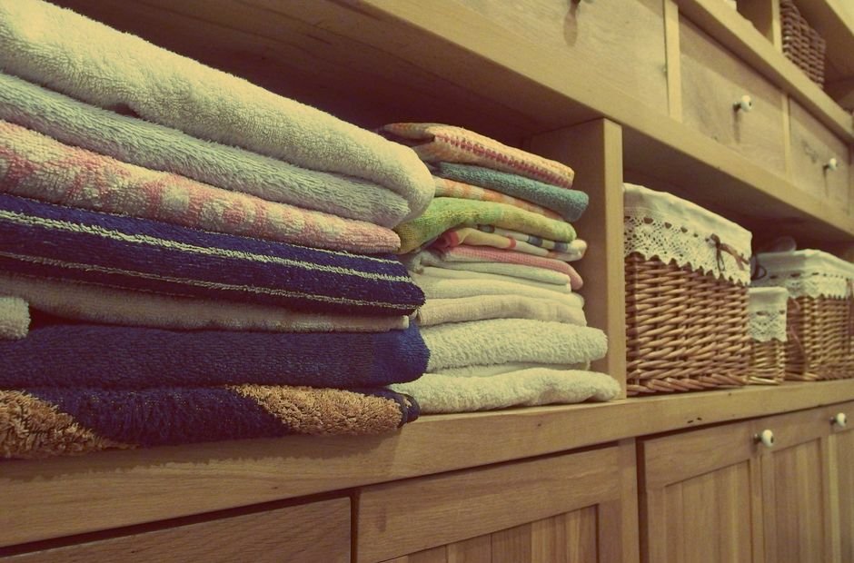 Stacks of blue, cream and patterned towels on the open shelves of a pale wooden linen cupboard beside two lidded wicker baskets