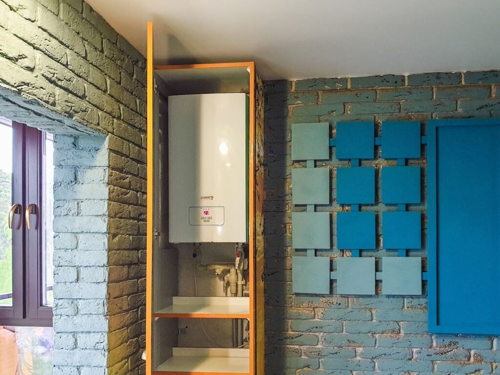 A wall-mounted water heater in an open cabinet with exposed supply pipework and valves beneath it