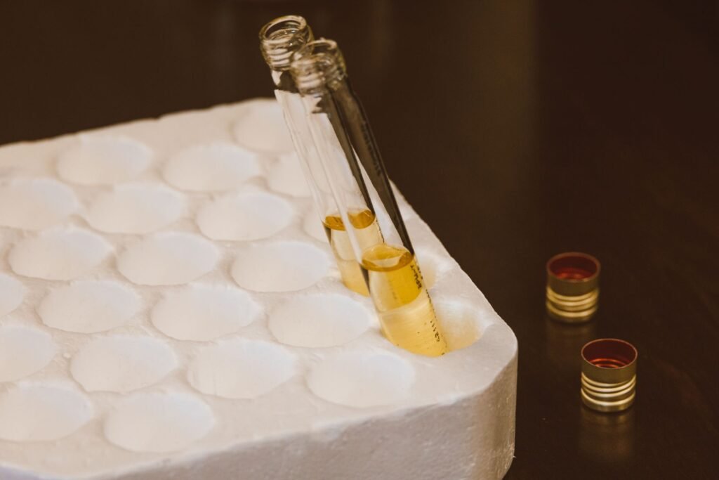 Two glass test tubes of amber liquid standing in a white foam rack beside small reagent caps
