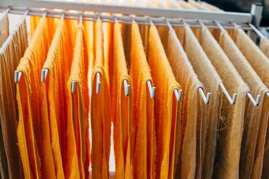 Orange and cream bath towels hanging over the white metal bars of an indoor folding clothes airer, backlit by a window