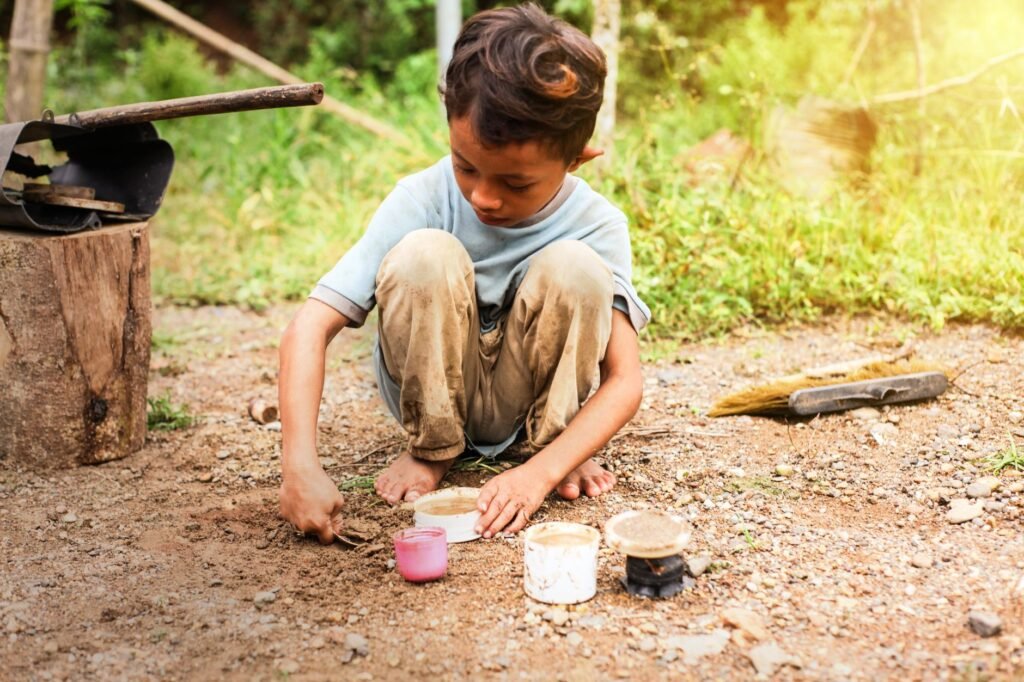 A boy crouching on dry dusty ground with his pale trousers ground in with soil at the knees and seat