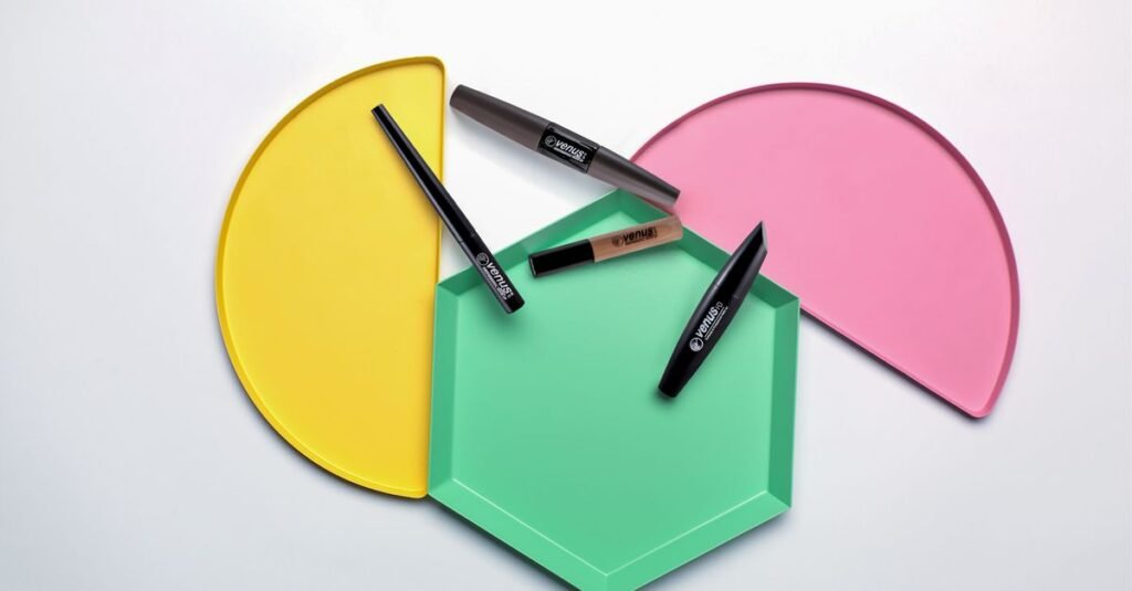 Four eyeliner products on coloured trays - a slim black pencil, two black liquid liner pens and a short nude tube with a brush applicator