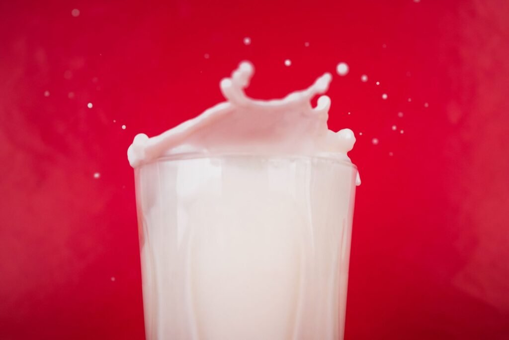 Milk splashing up over the rim of a tall glass and running down the outside, photographed against a bright red background