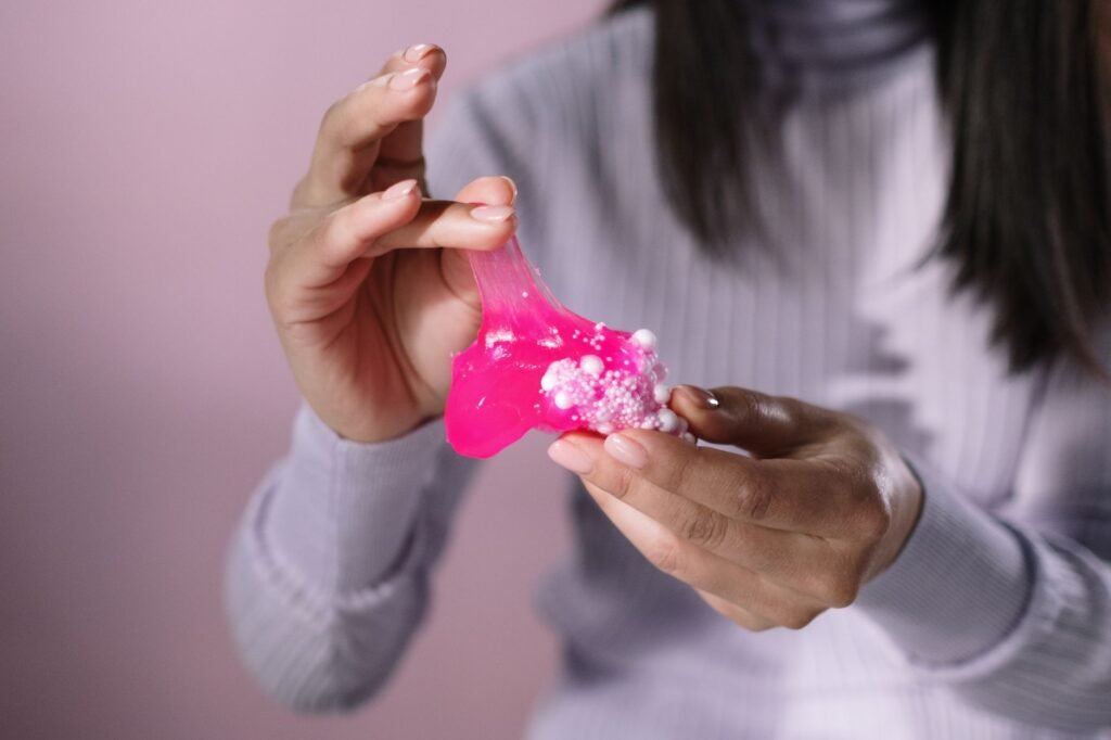 A person in a pale ribbed jumper stretching a piece of bright pink slime studded with white foam beads between two hands