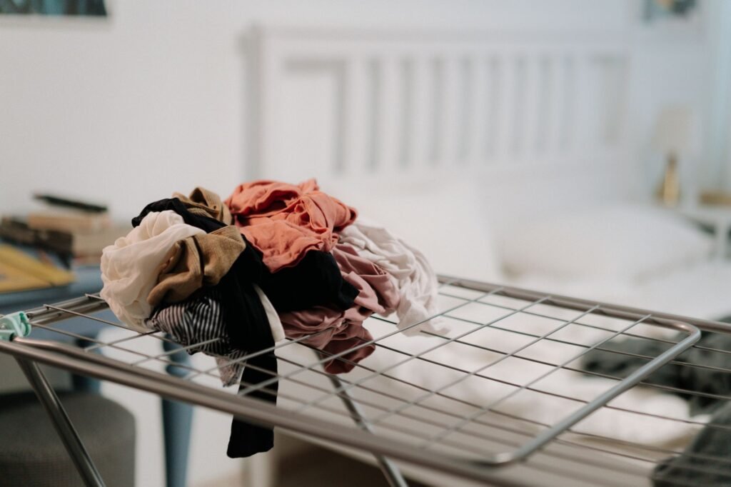 A bundle of damp washed laundry heaped together on an indoor drying rack in a bedroom, packed too tightly to dry