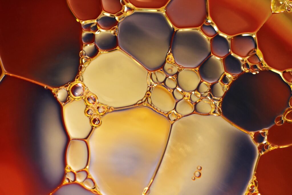 Macro view of golden oil beading into separate round droplets on a coloured liquid, refusing to mix with the water underneath