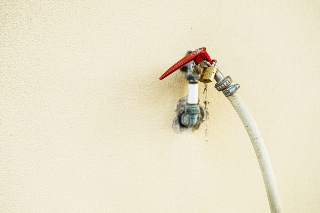A wall tap with a red lever handle and a hose screwed to it, water visibly escaping at the threaded joint, the connection behind most questions about how to stop a washing machine flood