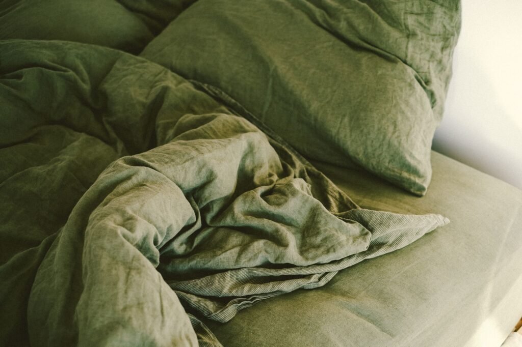 A rumpled olive-green duvet cover and matching pillowcase pushed back across a bed, the open hem of the cover visible