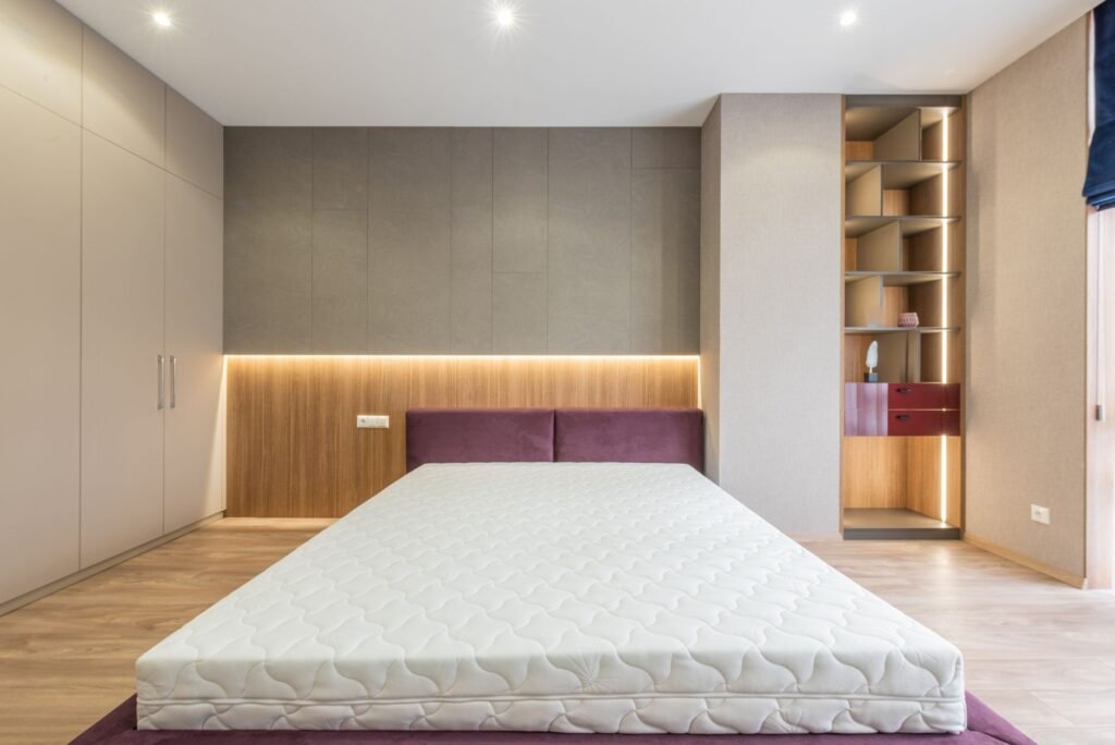 A stripped double bed in a modern bedroom with the bare quilted mattress exposed and no bedding on it