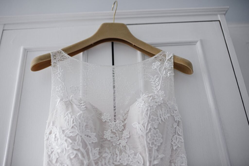 Back of an ivory floral-lace wedding gown on a wooden hanger against a white panelled door, a narrow beaded zip running down the centre