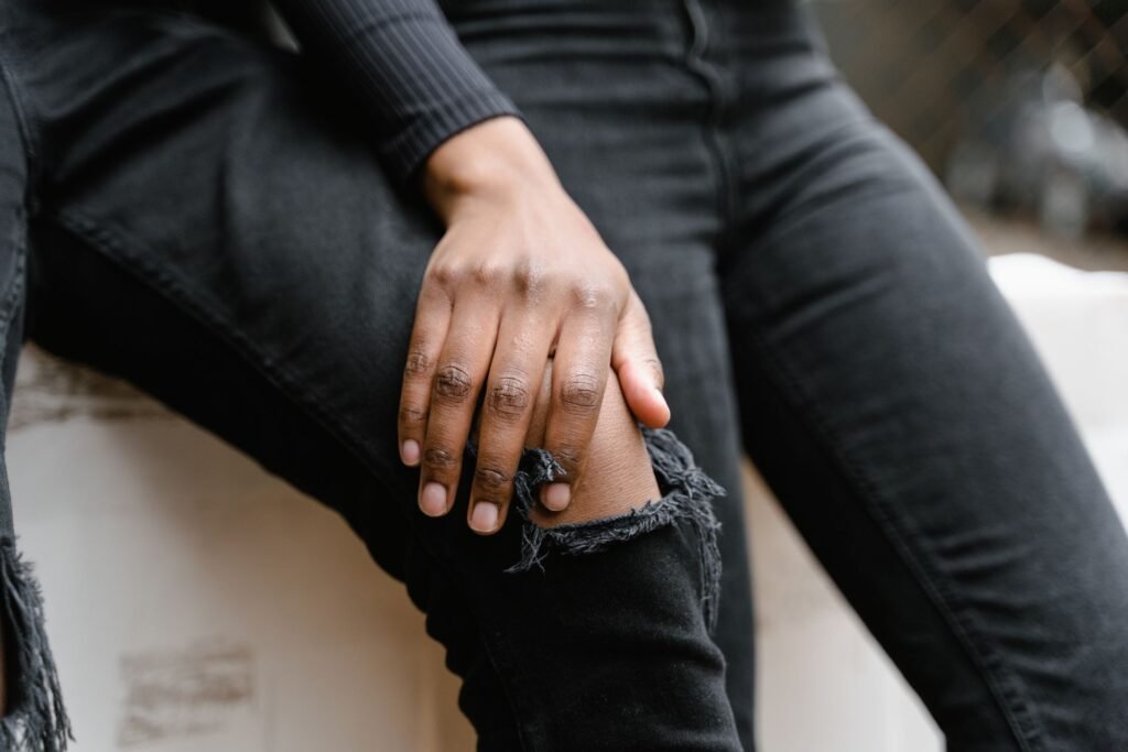 Close-up of a seated person resting a hand on the knee of washed-out black skinny jeans with a torn knee, the denim visibly greyer at the knee and thigh than at the seams