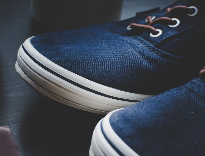 Close-up of two navy canvas sneakers with brown laces and metal eyelets, the white rubber foxing stripe already grey along its bottom edge