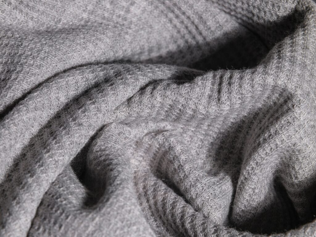 Close-up of soft grey fine-knit cashmere bunched into deep folds, showing ribbed and waffle stitch and the faint halo of loose fibre on the surface