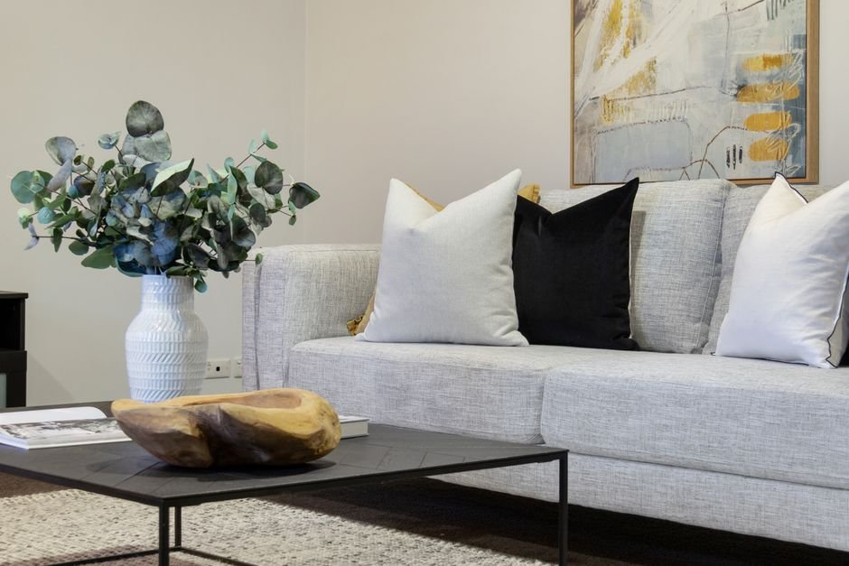 A pale grey fabric sofa with white, black and mustard square scatter cushions along the back, the kind of removable covers that shrink off their inserts