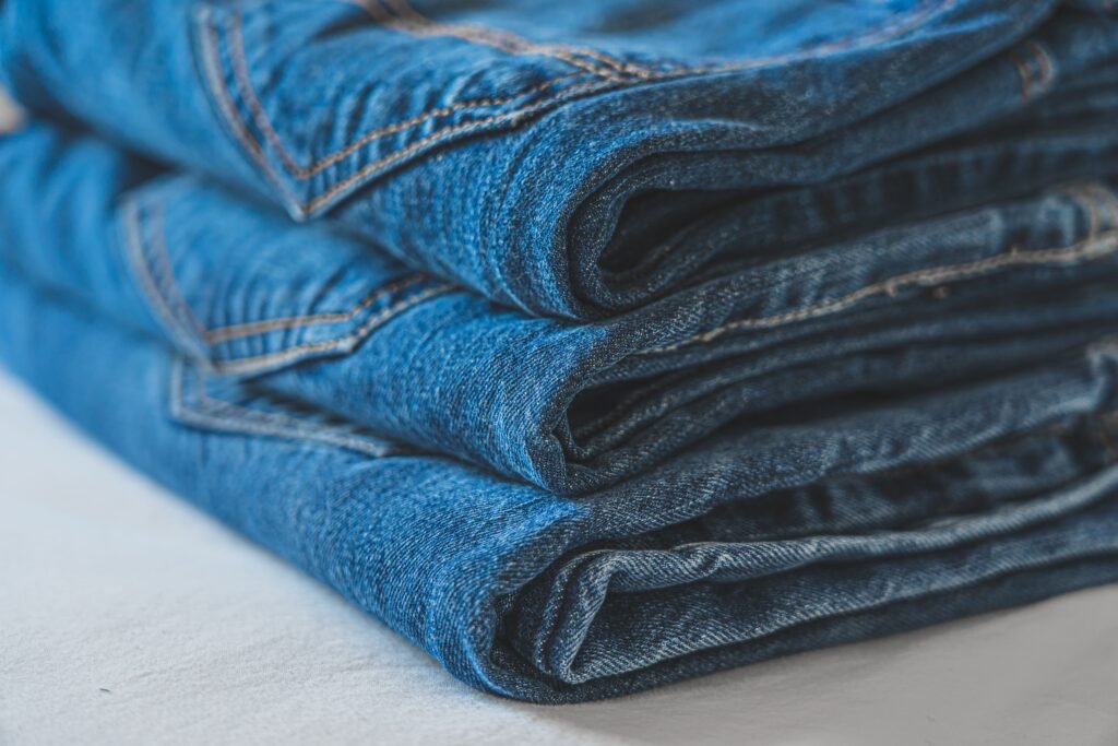 Three pairs of blue jeans folded in a stack, with gold topstitching, back pockets and pale wear lines showing along the fold creases