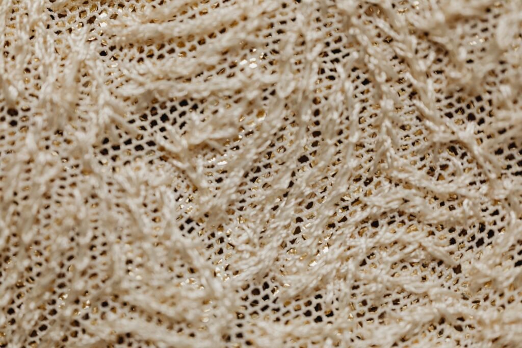 Close-up of cream open-work lace shot through with metallic gold thread, showing the open mesh and loose loops that catch