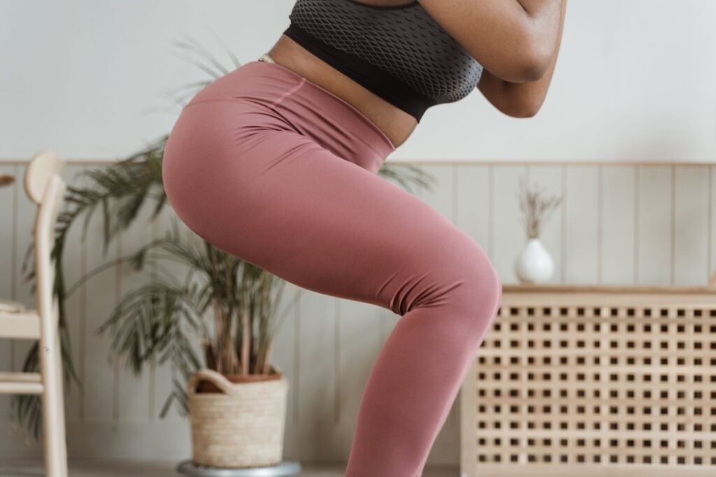 Close-up of a person in dusty pink high-waisted leggings and a black sports top mid-squat indoors, showing the waistband and the fabric creasing behind the knee