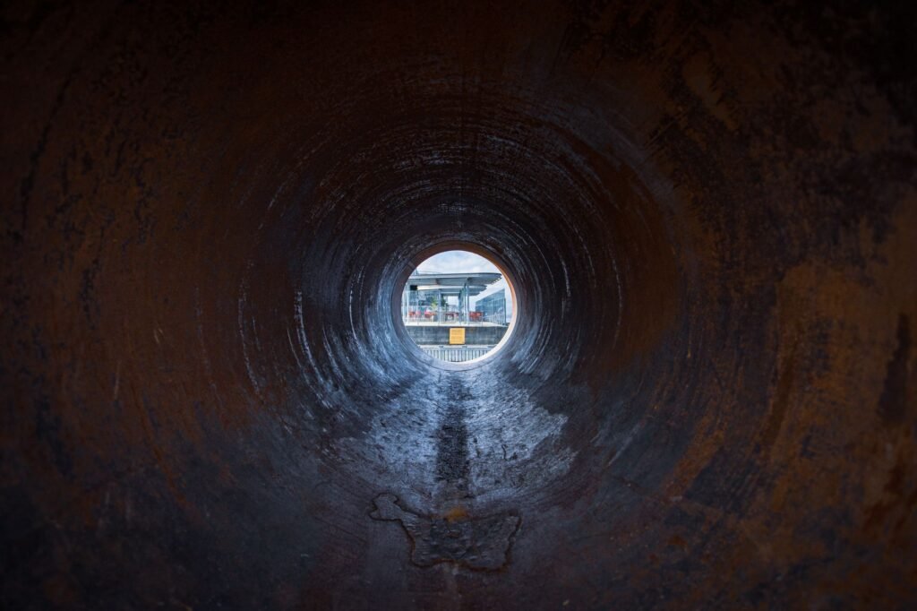 View along the inside of a rusted steel pipe towards a bright circular opening, the kind of sightline a duct camera returns