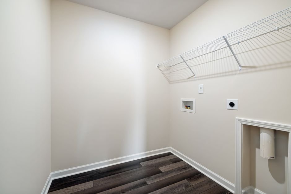 Empty laundry closet with a white wire shelf on brackets along one wall, above a recessed washer valve box, a dryer vent outlet and a power socket