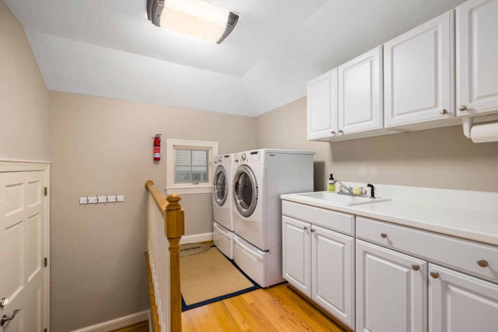 A white front-load washer and matching dryer raised on pedestals in a home laundry room with white cabinets and a utility sink