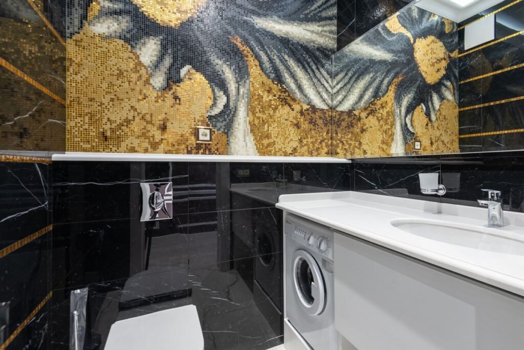 A front-load washing machine slotted under a white bathroom vanity worktop beside the basin, the kind of borrowed space a portable washing machine ends up in
