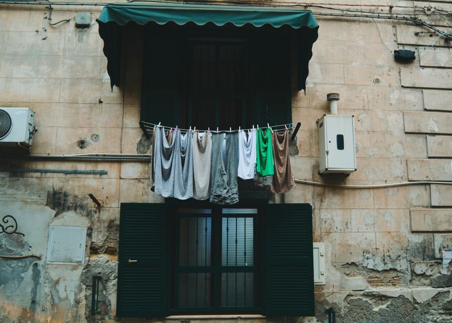 A single taut washing line pegged with pale vests and shirts strung across the front of a weathered stone building between two shuttered windows