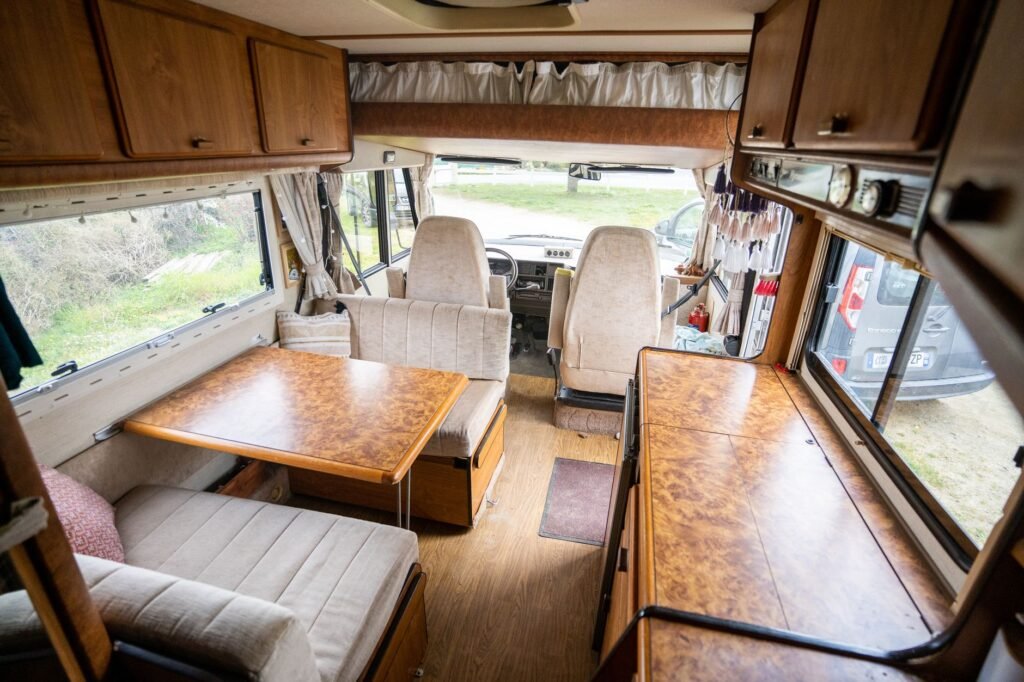 Interior of a Class C motorhome looking forward past a burl-wood dinette and galley worktop, the kind of space an RV washing machine has to be found inside