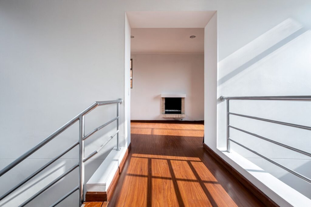 An upstairs landing with a polished hardwood floor and steel railings open over the stairwell, the kind of layout second floor laundry leak protection has to account for