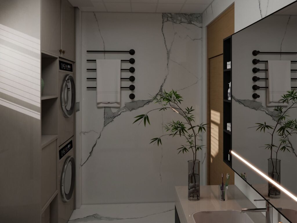 A front-load washer with a dryer stacked directly above it in an alcove beside a marble-tiled bathroom wall and towel rail