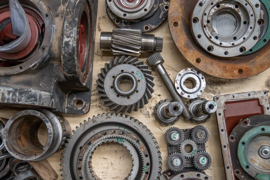 A stripped gearbox laid out on a workbench from above, showing a splined pinion shaft, a bevel gear, a large toothed ring gear, four small planet gears, bearing races and a cast aluminium housing