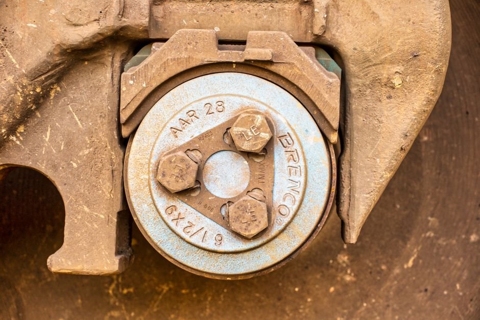A heavy industrial bearing end cap stamped BRENCO and AAR 28, held in a rusted cast housing by three hexagonal bolts, photographed straight on