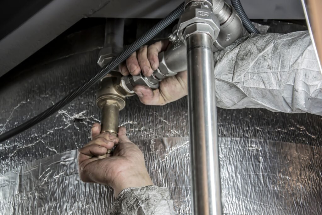 Two hands tightening a brass fitting onto a steel supply pipe behind an appliance during installation