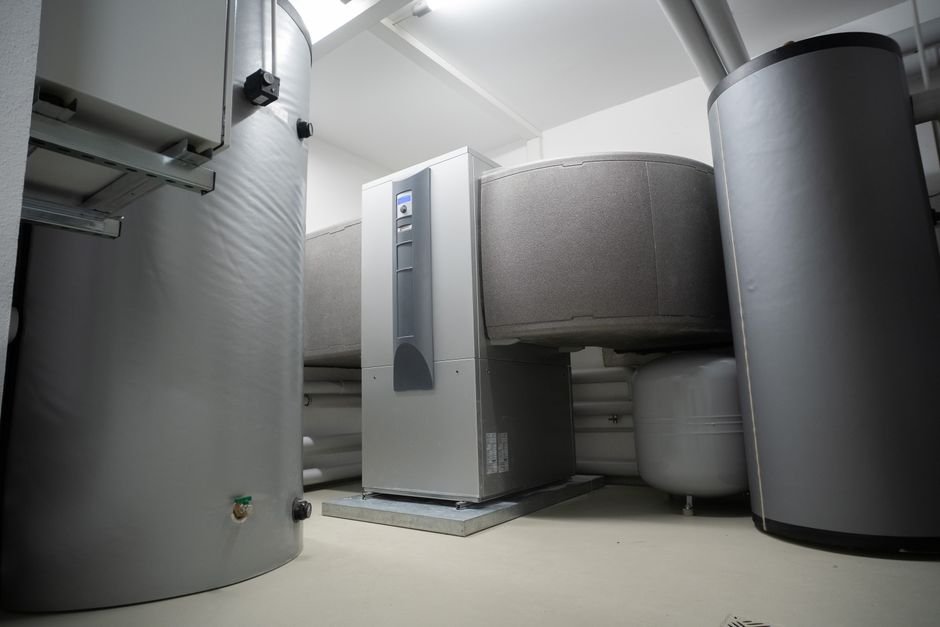 A domestic plant room with two insulated hot water storage cylinders either side of a heat pump indoor unit and a small expansion vessel